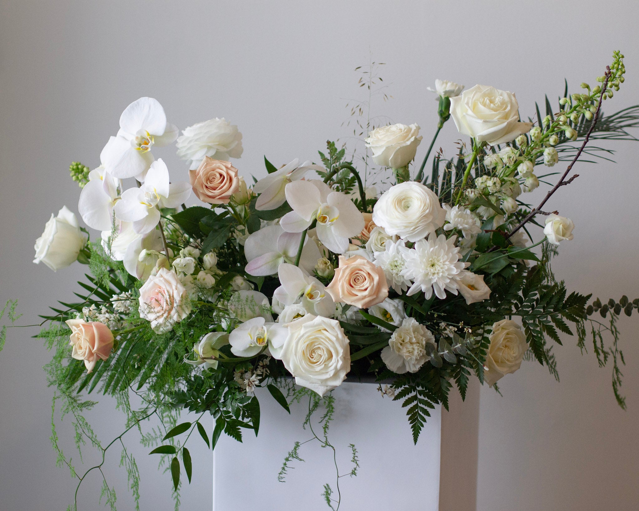 Casket spray for funeral with white roses, orchids, ranunculus, and more