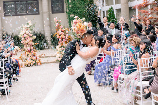 Couple kissing in front of a colourful floral arch by May Flowers. Photography by Ether Photography