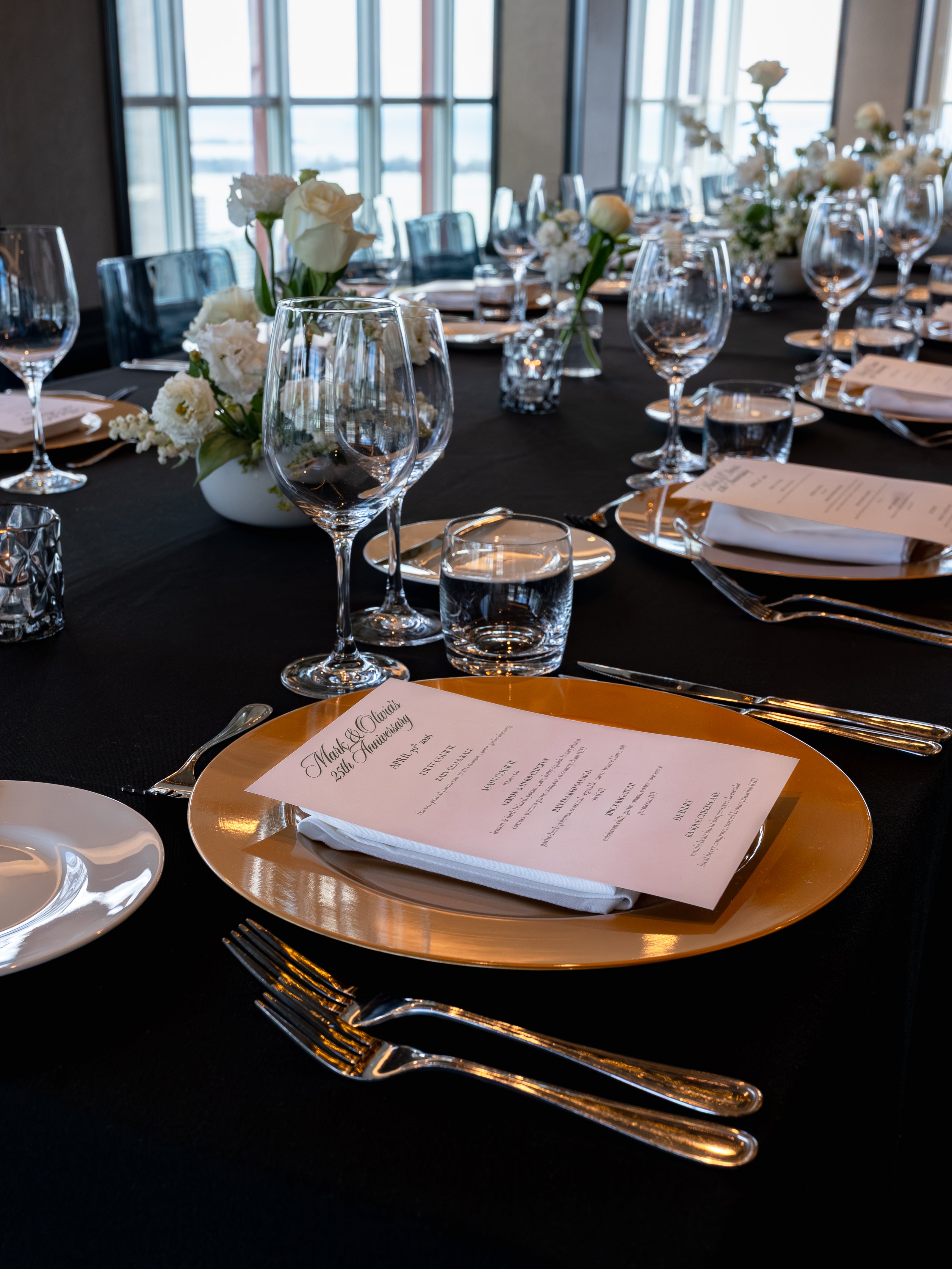 Elegant table setting with black tablecloth, gold charger plate, and white flowers.