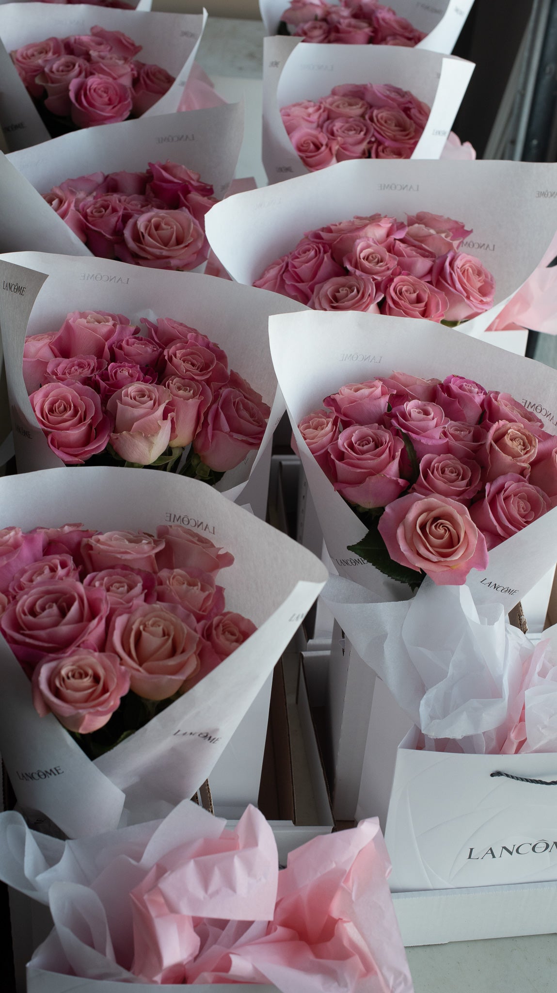 Bouquets of pink roses in white branded gift bags on a light background
