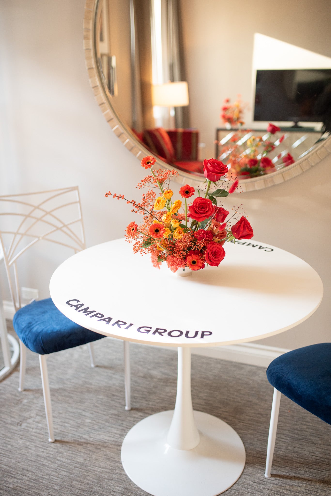 White table with a colorful flower arrangement in a room with chairs and a mirror.